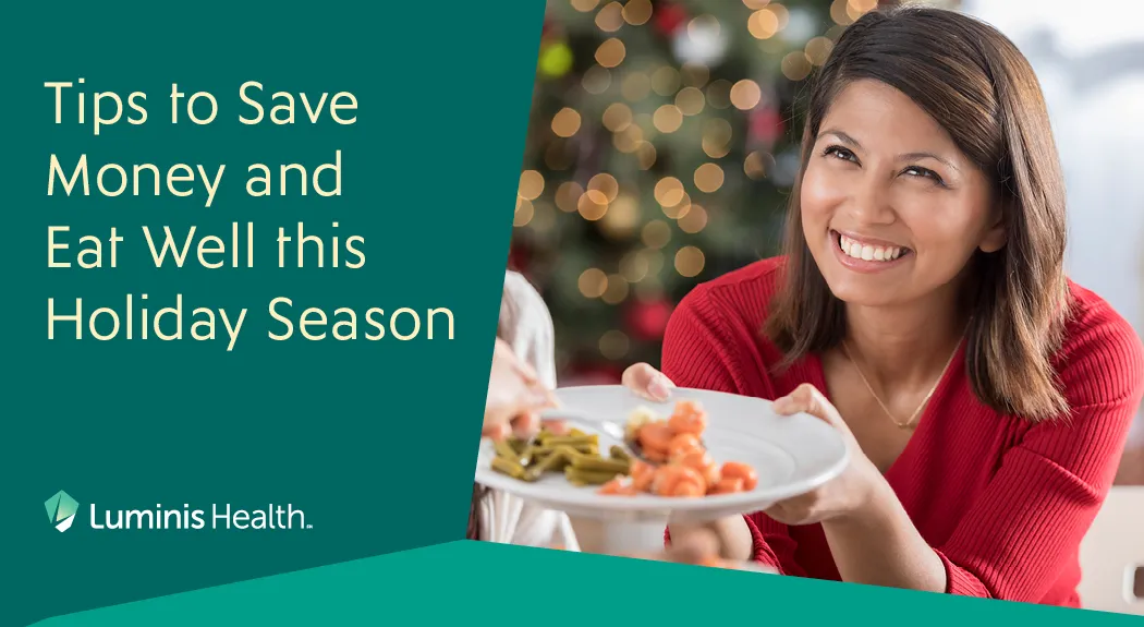 Tips to save money and eat well this holiday season - a woman smiling and holding a plate of holiday roasted vegetables.