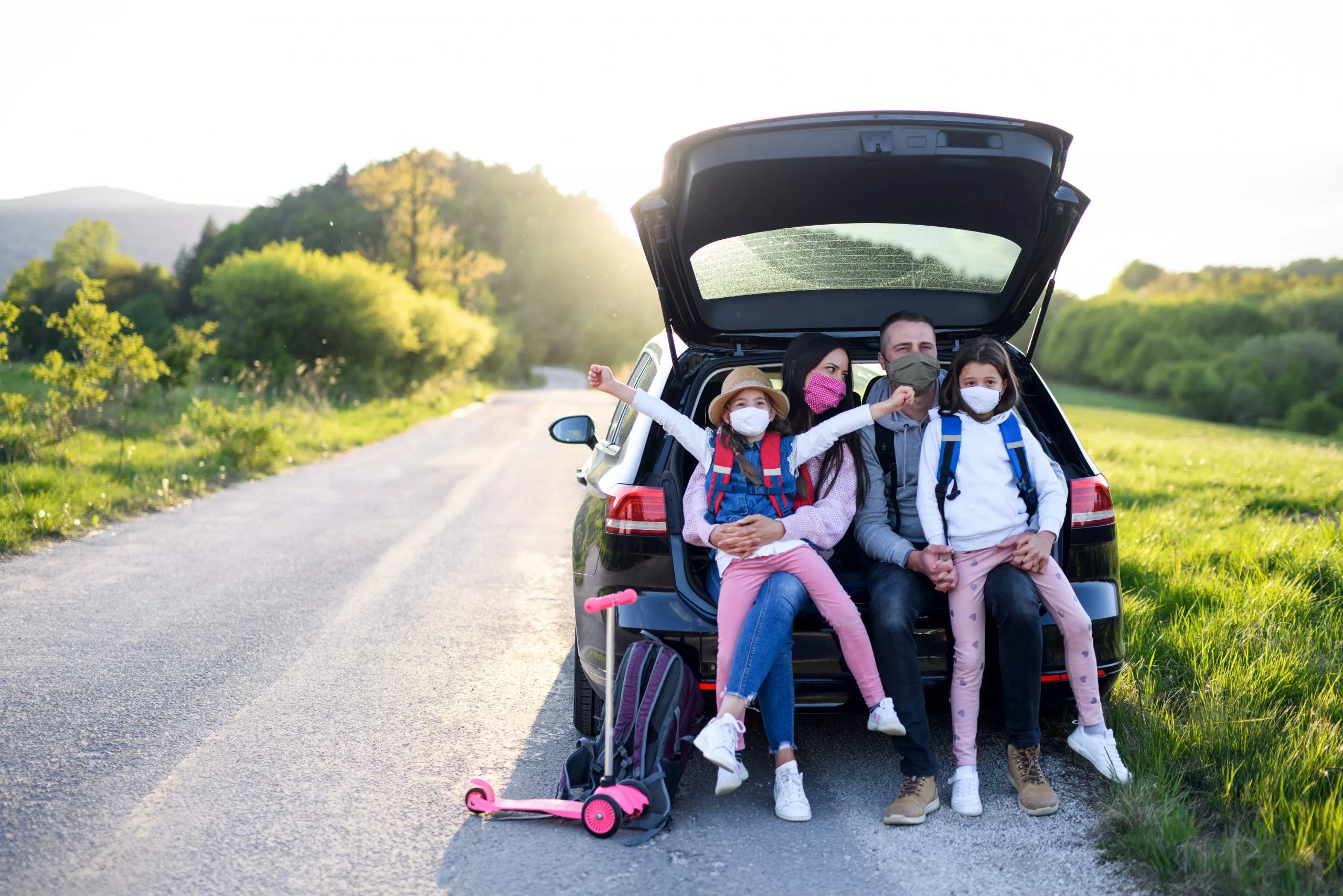 Family with two small daughters on trip outdoors in nature, wearing face masks.