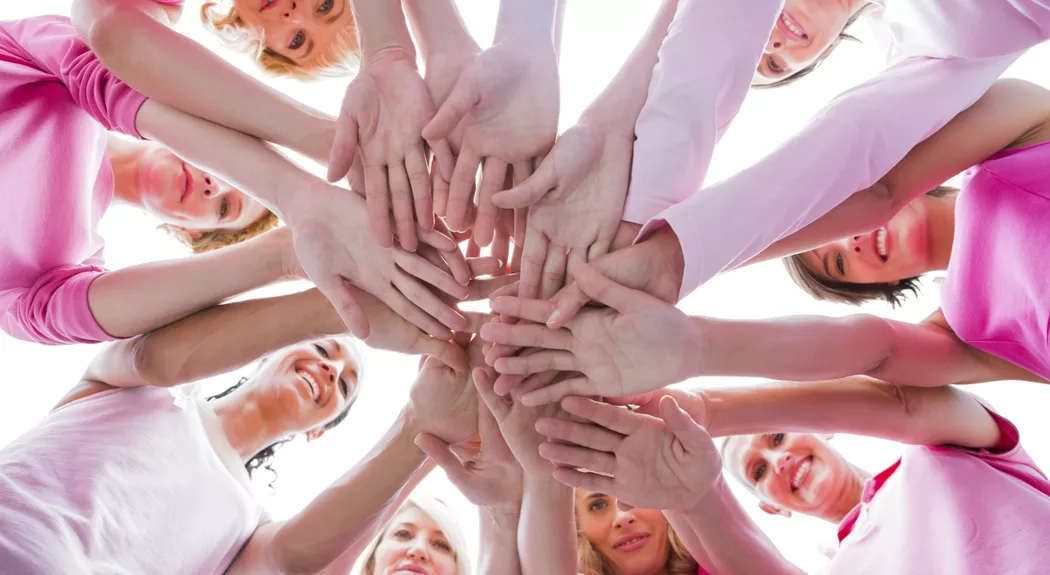 Diverse women smiling in circle wearing pink for breast cancer